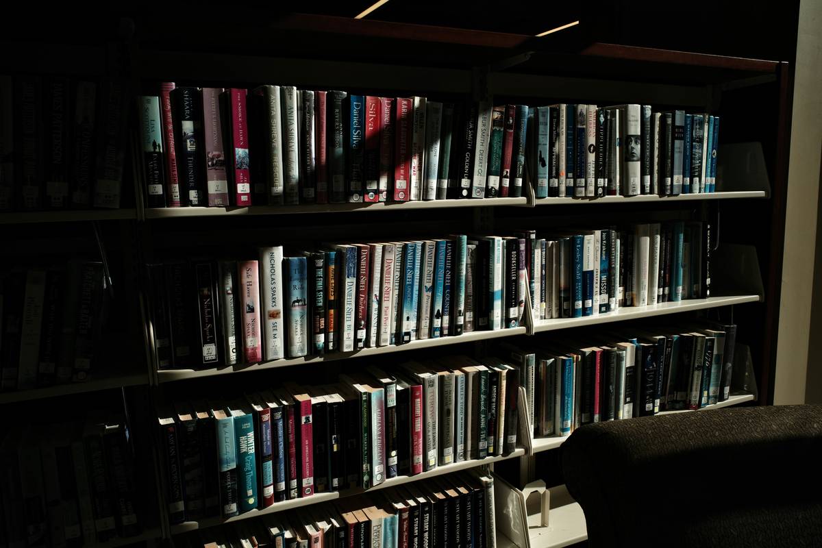 Stack of classic psychological thriller books including 'Rebecca' and 'The Turn of the Screw' on a dimly lit desk with a flickering candle