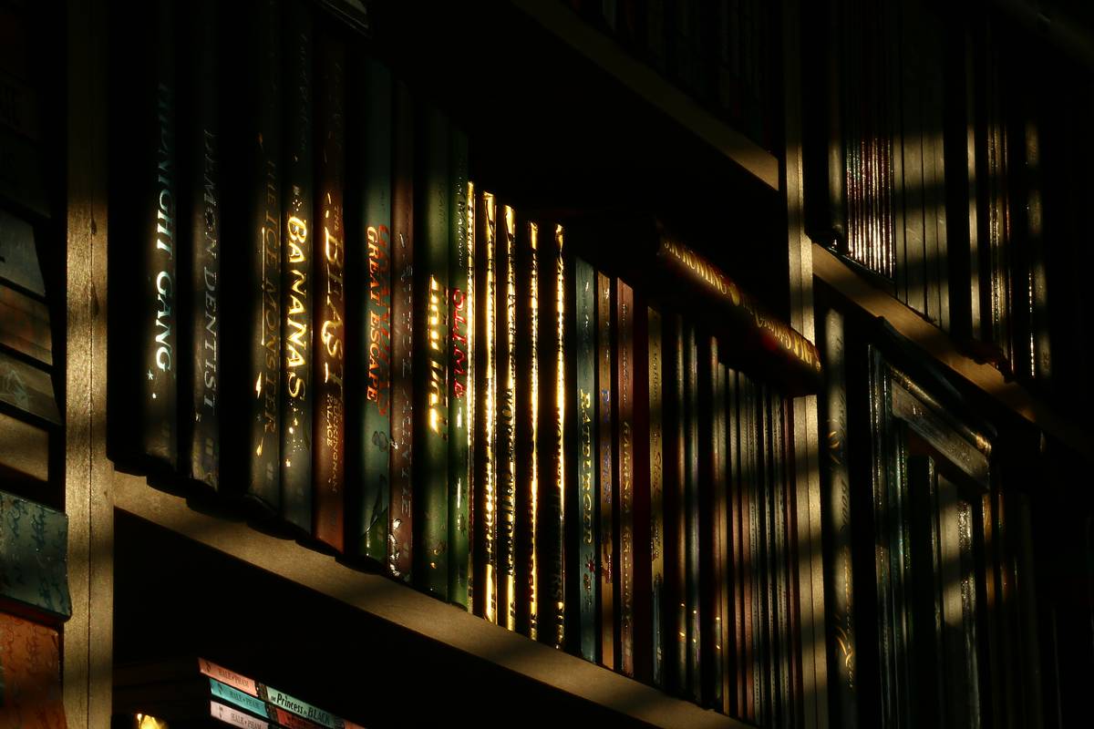 Stack of psychological thriller books for adults arranged beside a dimly lit desk lamp, evoking suspense and late-night reading